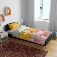 Yellow bedding set on bed with pink protea floral print and patterned central emblem, two pillows
