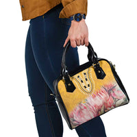 Yellow and pink floral handbag with black handles and crossbody strap, held near hip.
