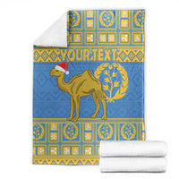 Folded blue blanket with camel and Santa hat, gold geometric and laurel border design