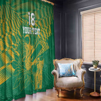 Green printed window curtains with gold cricket player artwork and rays, hanging beside window.