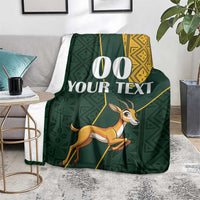Green springbok blanket with yellow patterned trim and custom text, on floor