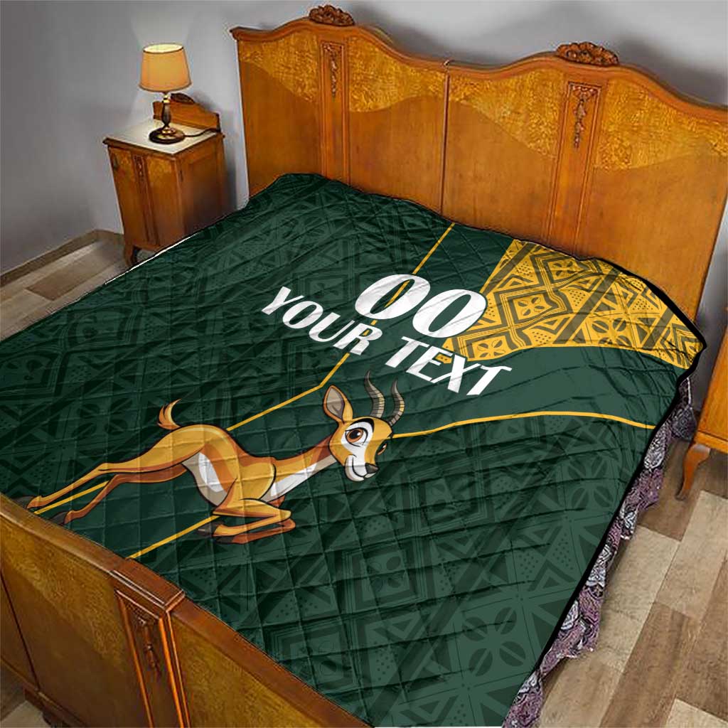 Dark green quilt on bed with yellow Kente-style edge, jumping springbok, “00 YOUR TEXT”