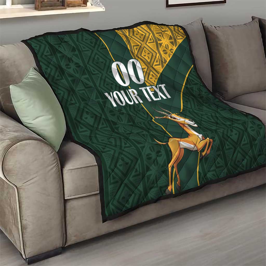 Dark green quilt on sofa with yellow Kente-style corner, jumping springbok, “00 YOUR TEXT”