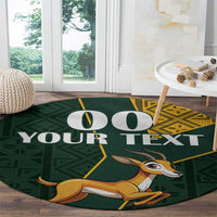 Round area rug, dark green with springbok illustration, “YOUR TEXT” and yellow kente border