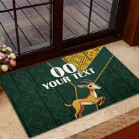 Green rubber doormat with custom 00 YOUR TEXT and springbok illustration over geometric motifs