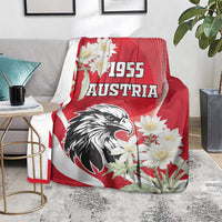 Red Austria blanket on gray couch with eagle artwork, “1955” lettering, and white flowers