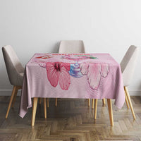Pink Christmas tablecloth with floral artwork and red text, on dining table with chairs