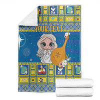 Blue Christmas blanket with angel graphic, folded with stacked white bedding pieces