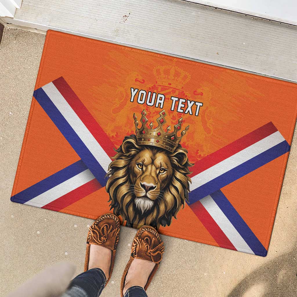 Orange rubber doormat showing crowned lion head, Dutch flag stripes, and 'YOUR TEXT'.