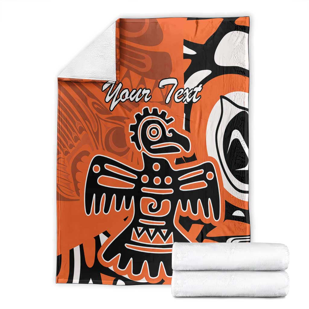 Personalized orange Haida eagle blanket folded with stacks of white fabric, “Your Text” visible