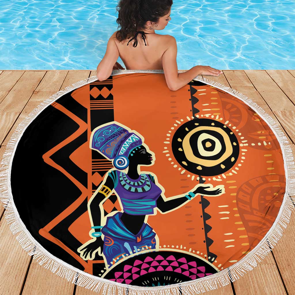 Round orange beach blanket featuring African woman graphic, black symbols, and white fringe