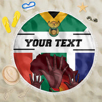 Round flag-style beach blanket with fringe, 'YOUR TEXT' and hands emblem on sand