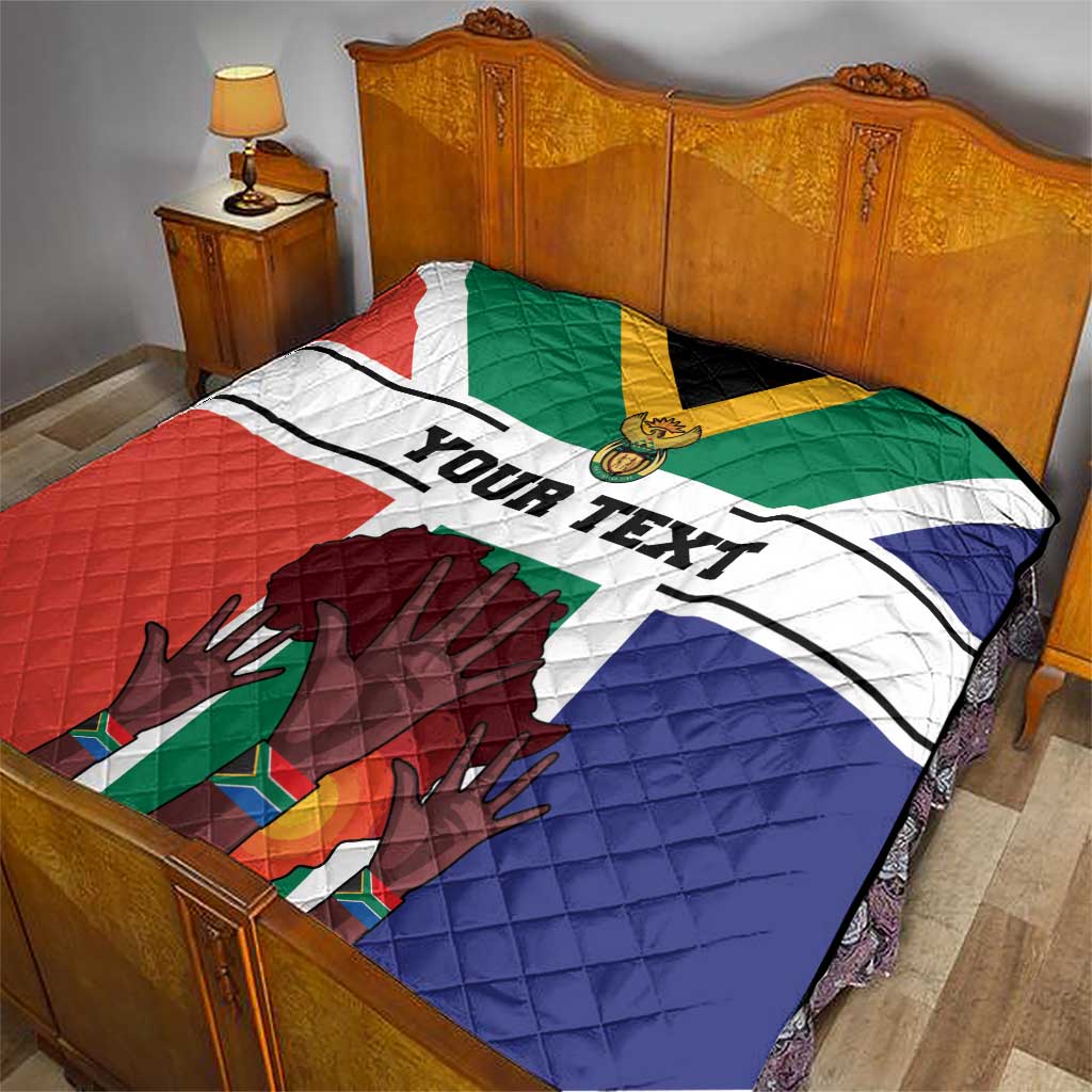 Personalized quilt on bed featuring South Africa flag colors and 'YOUR TEXT' over quilted hands