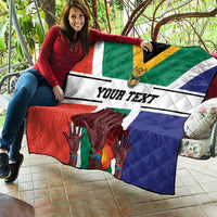 Personalized South Africa flag quilt draped on couch with 'YOUR TEXT' and quilted hands