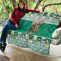 Green quilted blanket spread on couch with Aztec-style border and Mexico crest in center.