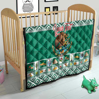 Green quilted blanket on wooden crib with Aztec-style border and Mexico crest.