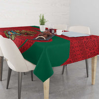 Red and green folk-pattern tablecloth draped over dining table with dinnerware