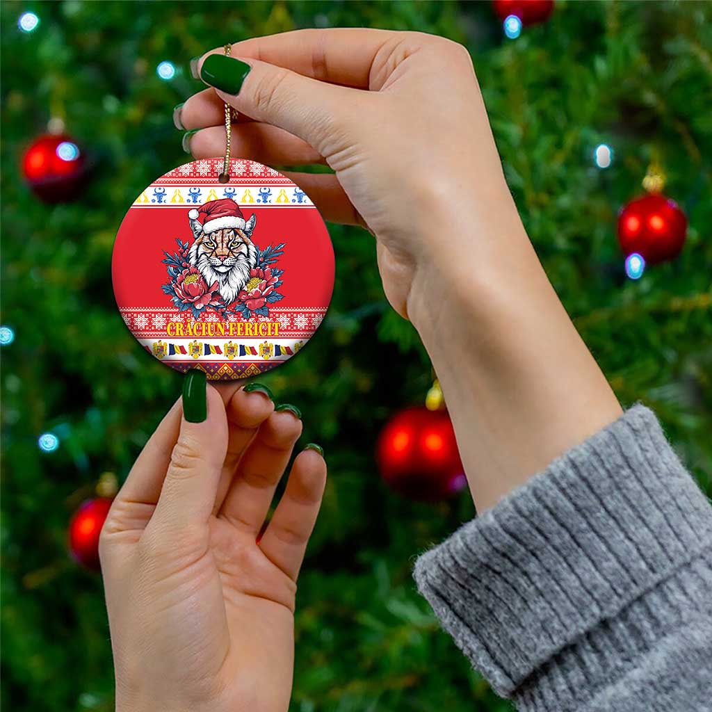 Red round ceramic Christmas ornament with Eurasian lynx in Santa hat and peony flowers, held by hand