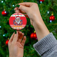 Red round ceramic Christmas ornament with Eurasian lynx in Santa hat and peony flowers, held by hand