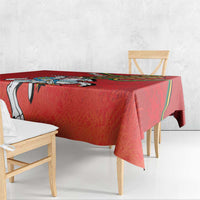 Red coat of arms tablecloth draped over a wooden table, hem and corner visible.