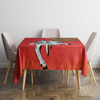 Red coat of arms tablecloth on table with four upholstered chairs, front view.