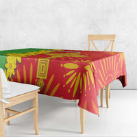 Square folk-pattern tablecloth draped over dining table in red and green with yellow motifs