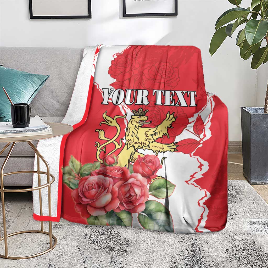 Red and white personalized blanket with roses and lion crest, 'YOUR TEXT' on sofa.