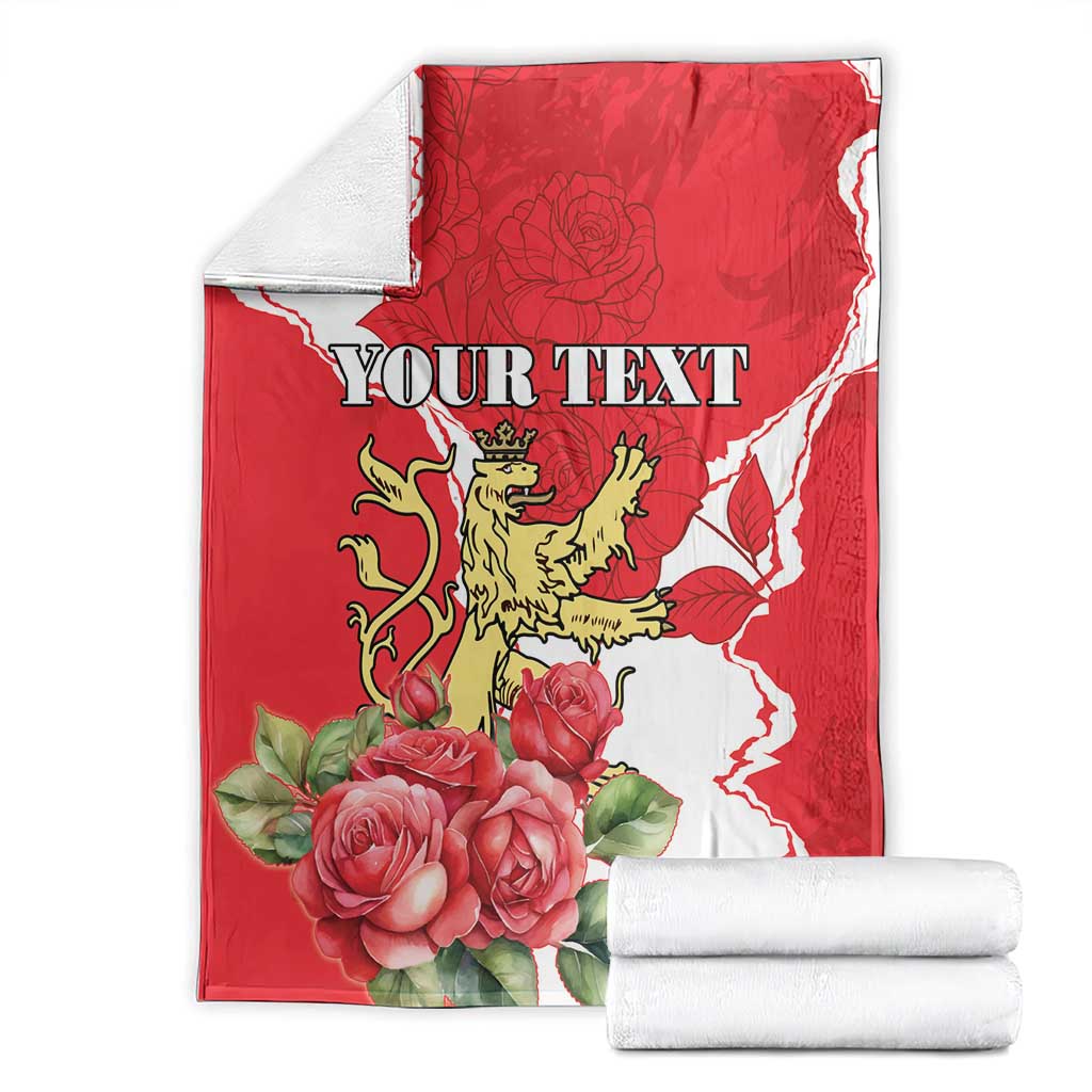 Red and white personalized blanket with roses, lion crest, and 'YOUR TEXT', folded with stacks.