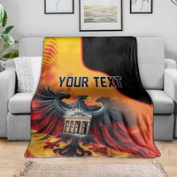 Personalized blanket draped over sofa; “YOUR TEXT” over eagle and Berlin Wall art.