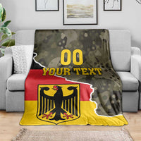 Green camo blanket on sofa with red stripe, yellow panel, and black coat of arms with “YOUR TEXT”