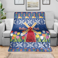Blue Christmas blanket with windmill and tulip flower print, draped over a gray sofa.