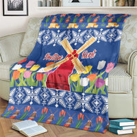Blue Christmas blanket with windmill and tulip flower print, shown close on a couch.