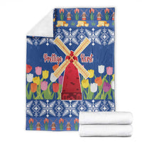 Blue Christmas blanket with windmill and tulip flower print, folded with rolled white stacks.