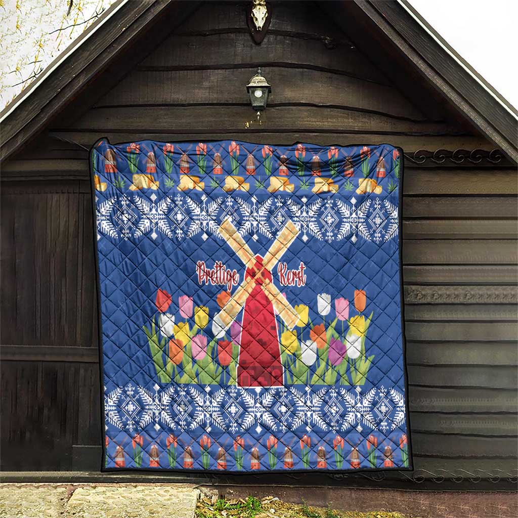 Blue quilt displayed on wooden wall with windmill cross, tulips, and snowflake border.