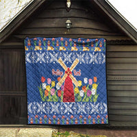 Blue quilt displayed on wooden wall with windmill cross, tulips, and snowflake border.