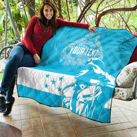 Personalized blue quilt with Honduras bird graphic and stars, laid over seating