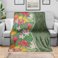 Green floral blanket draped on a sofa, featuring pink and yellow flowers with leaf motifs
