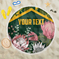 Green round beach blanket with tropical floral print, yellow Kente-style border, fringed edge