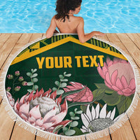 Green round beach blanket with tropical print and yellow Kente-style border, fringed edge