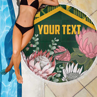 Green round beach blanket with tropical print, yellow Kente-style border, white fringed edge