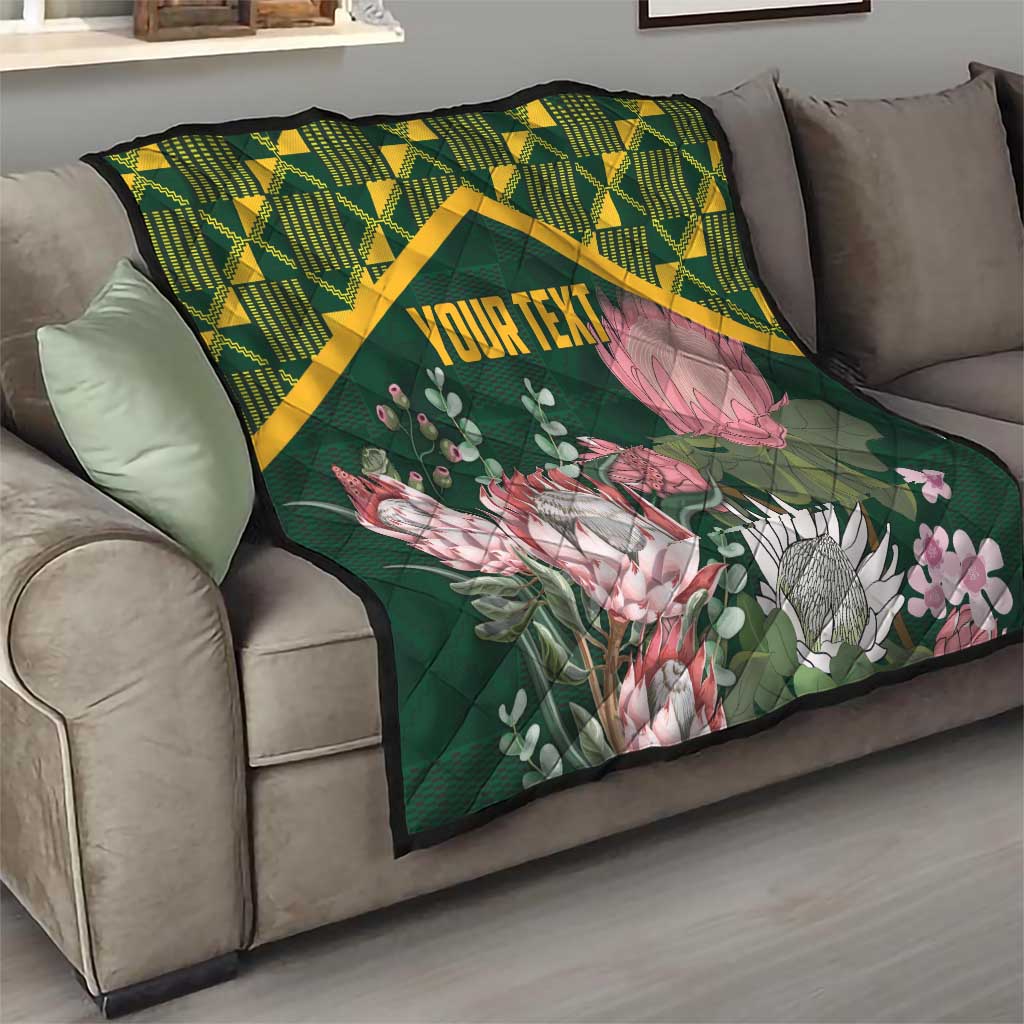 Green quilt with yellow kente border, pink protea flowers, and “YOUR TEXT” on couch