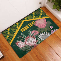 Green rubber doormat with geometric Kente border, pink protea bouquet, 'YOUR TEXT' in yellow
