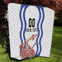 White quilt laid on grass showing blue wavy emblem, custom text, and carnation dragon design.