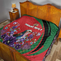 Personalized quilt laid on bed with red-and-green swirl pattern, purple flowers, and “YOUR TEXT”