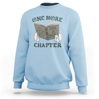 Light blue sweatshirt with front graphic of an open book, candles, and “ONE MORE CHAPTER”