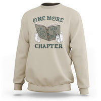 Sand sweatshirt with front graphic of an open book, candles, and “ONE MORE CHAPTER”