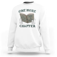 White sweatshirt with front graphic of an open book, candles, and “ONE MORE CHAPTER”