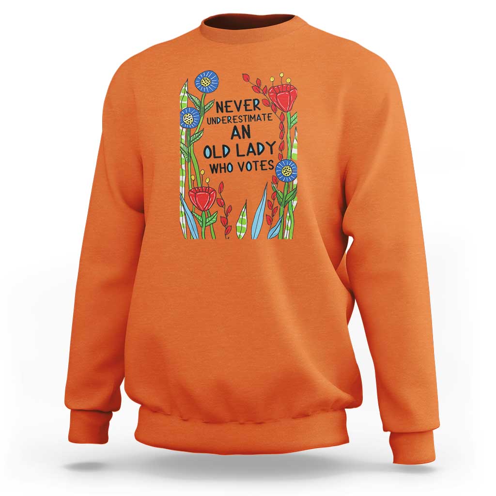 Orange crewneck sweatshirt with “Never Underestimate an Old Lady Who Votes” graphic