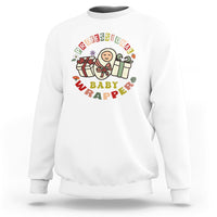 White crewneck sweatshirt with colorful “Professional Baby Wrapper” nurse cartoon graphic