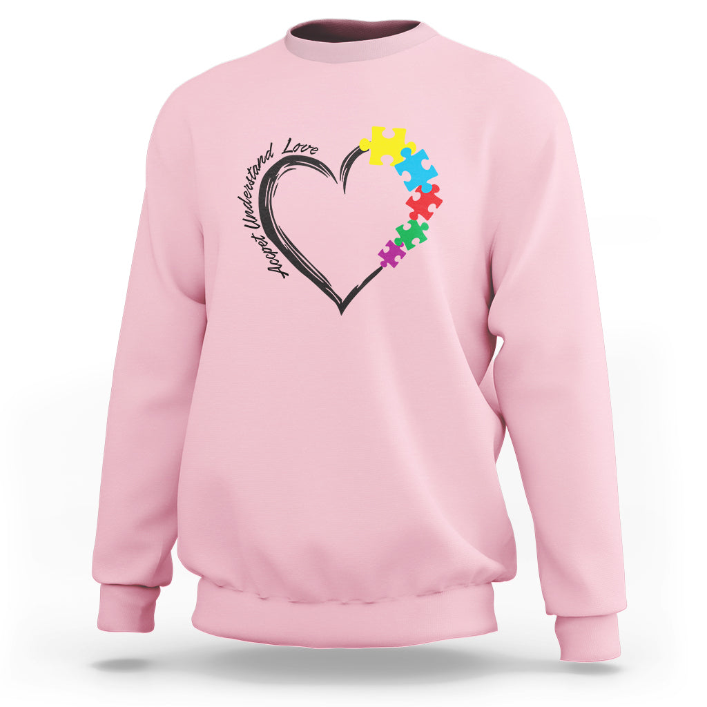 Light pink autism awareness sweatshirt with heart-and-puzzle graphic on chest.